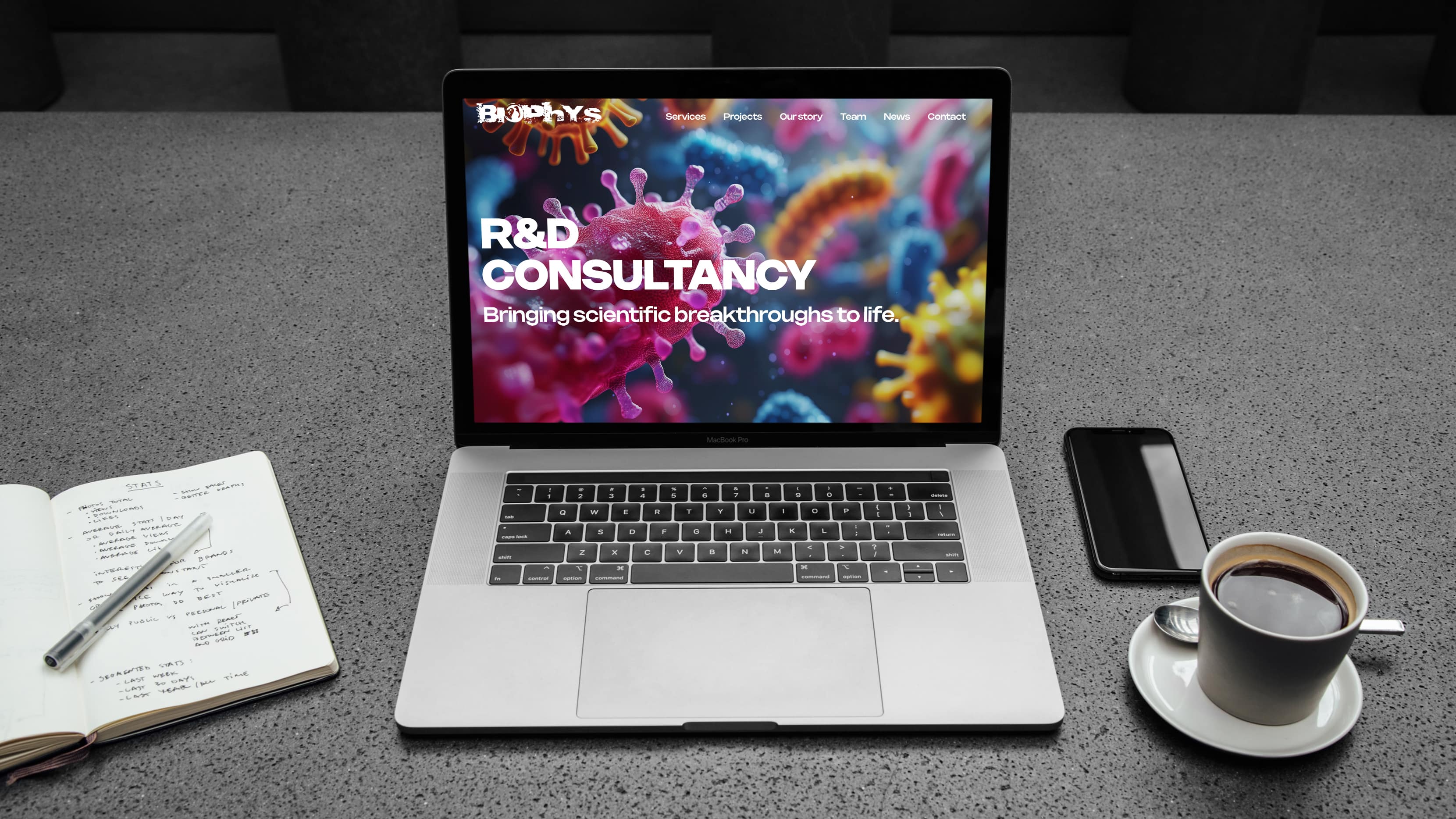 Laptop on a desk displaying the Biophys life sciences consultancy WordPress website homepage, with a notebook, phone and coffee nearby.